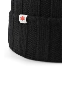Bonnet en tricot noir avec une texture côtelée, arborant une petite étiquette en forme de feuille d'érable rouge sur fond blanc. Matériau en laine doux et forme arrondie.