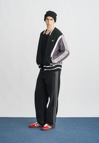 Μαύρο πλεκτό σακάκι με γκρι λεπτομέρειες και λευκές ρίγες, μαύρο πουκάμισο, φαρδιά μαύρα τζιν και κόκκινα αθλητικά παπούτσια με λευκές ρίγες.