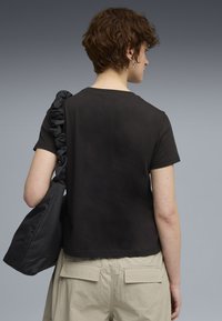 Zwart T-shirt met korte mouwen en een ronde hals, gedragen met een zwarte tas met textuur en een gerimpelde band. Lichtbeige cargobroek zichtbaar.
