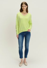 Limeta zelena, oversized, v-izrez džemper od mekog materijala, uparen s uskim plavim trapericama i bež balerinkama. Jednostavan, ležeran izgled.