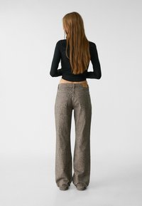 Beige široké džíny s leopardím potiskem, spárované s přiléhavým černým topem s dlouhým rukávem, pohled zezadu.