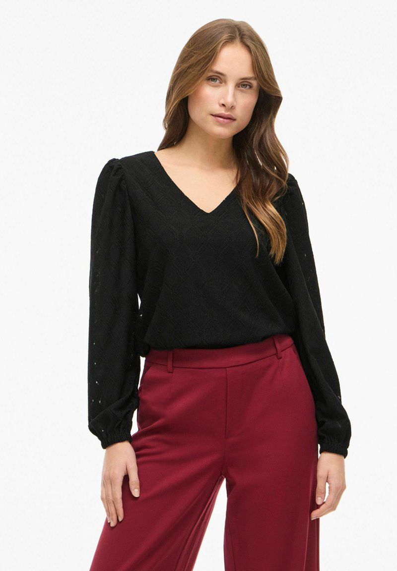 Top nero a V con motivo a losanghe e maniche lunghe a sbuffo, abbinato a pantaloni bordeaux a vita alta in taglio dritto.