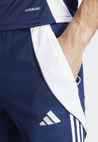 Marineblauwe sportshorts met witte accenten, gemaakt van vochtafvoerend materiaal, met een zijzak en drie diagonale strepen nabij de zoom.