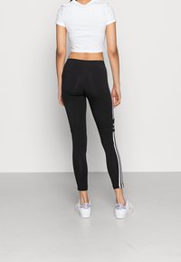 Leggings neri con strisce bianche ai lati, realizzati in materiale elasticizzato. Abbinati a una t-shirt bianca corta e sneakers con dettagli viola.