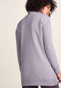 Light purple sweatshirt with a high collar, side zipper detail, long sleeves, and ribbed cuffs. Soft, textured fabric.