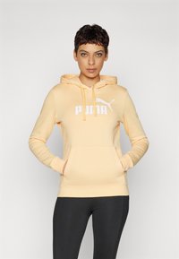 PUMA mikina svetložltá s predným vreckom, kapucňou so šnúrkami a bielym logom. Má dlhé rukávy a voľný strih.