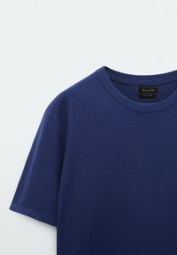 Granatowa koszulka z krótkim rękawem wykonana z fakturowanej tkaniny, z okrągłym dekoltem i metką wewnątrz kołnierza.