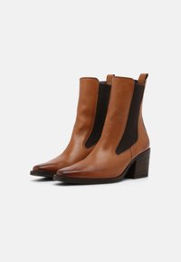 Bottines en cuir brun avec des panneaux latéraux élastiques noirs, bout pointu et un talon en bois moyen. Texture lisse avec un design minimaliste.