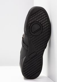 Chaussures noires avec une semelle en caoutchouc texturé, présentant un design épuré, un dessus en cuir lisse et un matériel de fermeture éclair visible sur le côté.