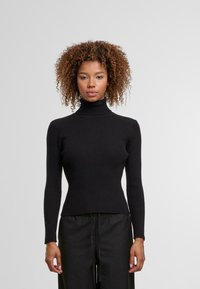 Czarny prążkowany sweter z golfem, posiadający długie rękawy, dopasowaną sylwetkę i teksturowany materiał. Zestawiony z luźnymi czarnymi spodniami.