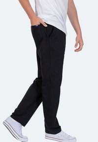 Schwarze Sweatpants mit geradem Schnitt, seitlichen Taschen und subtiler Markenkennzeichnung, kombiniert mit weißen Sneakers vor einem hellgrauen Hintergrund.