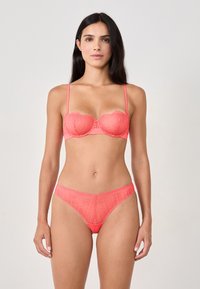 Koronkowy stanik w kolorze koralowym z falbaniastymi krawędziami i regulowanymi ramiączkami, w komplecie z pasującymi koronkowymi majtkami, posiadającymi teksturowany, wzorzysty design.