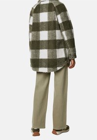 Chaqueta de cuadros difusos en patrón de check oliva y blanco, con un corte relajado, hem redondeado y dos bolsillos frontales, combinada con pantalones verde claro.