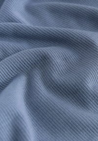 Țesătură ribbed de un albastru deschis moale, cu linii verticale fine texturate și pliuri delicate care creează umbre și adâncime.