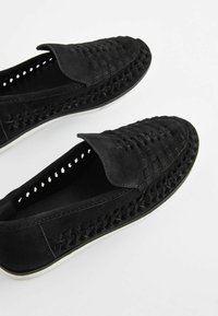 Black suede slip-on shoes featuring woven detailing and a textured upper, with a white rubber sole and accent stitching.