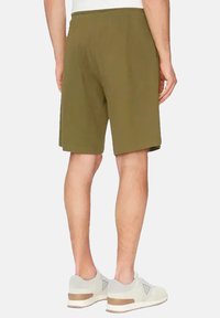 Olijfgroene shorts van zacht materiaal, met een elastische tailleband en een relaxte pasvorm. Gepaard met lichtgrijze sneakers met bruine accenten.