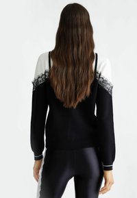 Pull noir et blanc avec des accents en dentelle, manches longues et poignets côtelés, associé à des leggings noirs, mettant en valeur la texture et le design.