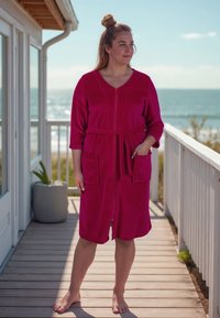 Accappatoio di un brillante colore rosa, con zip frontale, maniche a tre quarti, vita affusolata e due tasche a toppa. Tessuto morbido, design al ginocchio.