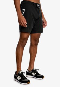 Svarta idrottsshorts med elastisk midja och RVCA-logotyp, kombinerat med svarta och grå sneakers med en vit N-logotyp och gummisulor.