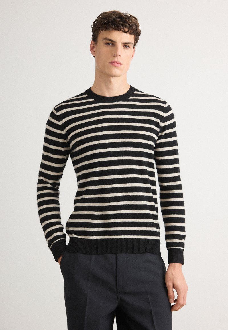 Suéter a rayas negras y crema con cuello redondo y puños acanalados. Textura suave, diseño ajustado, exhibido con pantalones oscuros.