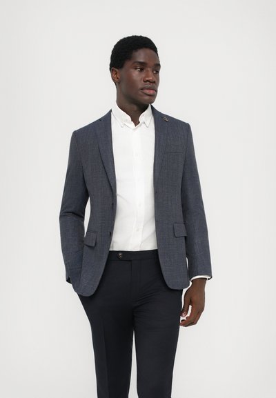 Navy kariertes Blazer aus strukturiertem Stoff, mit einem Einzelknopf, Schlagkragen und zwei Fronttaschen, getragen über einem weißen Hemd.
