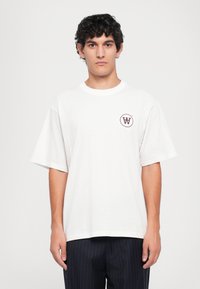 Hvit bomulls T-skjorte med rund hals og korte ermer, med en burgunder logo på venstre side. Enkel, avslappet passform.