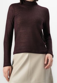 Pull col roulé bordeaux à manches longues en maille légère et texturée. Ourlet raccourci avec une coupe slim, associé à une jupe beige clair.