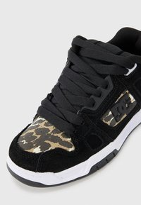 Black sneaker with suede material, featuring a beige and black leopard print toe cap, black laces, and a white sole with black accents.