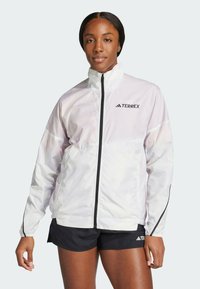 Giacca leggera bianca con colletto alto, zip frontale e dettagli neri. Presenta un logo del marchio sul petto e polsini elasticizzati.