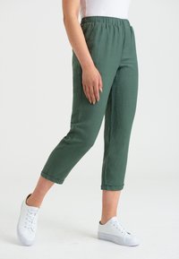 Gröna byxor med elastisk midja och rak stil, trekvartslängd. Försedda med vita sneakers, tillverkade av ett mjukt och lätt tyg.