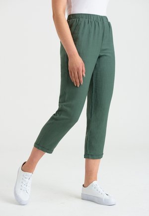 Pantalon vert à taille élastiquée, coupe droite et longueur trois quarts. Porté avec des baskets blanches, en tissu lisse et léger.