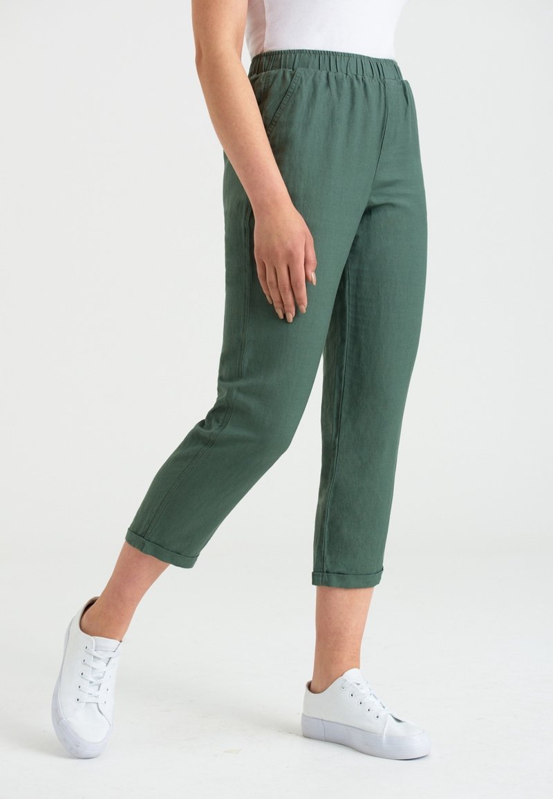 Gröna byxor med elastisk midja och rak stil, trekvartslängd. Försedda med vita sneakers, tillverkade av ett mjukt och lätt tyg.