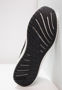 Semelle de chaussure de sport noire avec un motif texturé, mettant en avant des accents blancs et un logo Adidas bien visible. Positionnée sur une surface lisse.