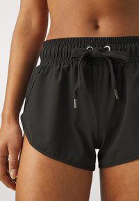 Schwarze Badehosen mit elastischem Bund, verstellbarem Kordelzug und Seitentaschen. Glattes Material mit lockerer Passform und abgerundetem Saum.
