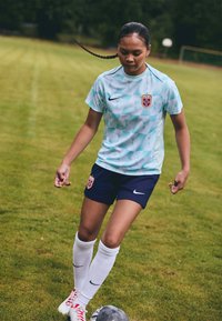 Nike fotbaltrøye i lyseblå diamantmønster, marineblå shorts, hvite knelange sokker, sko med røde detaljer, fokusert på ballen på gressbane.