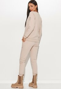 Beżowa bluzka z długim rękawem i dopasowane spodnie wykonane z miękkiego materiału, z prążkowanymi mankietami. Brązowe botki za kostkę z grubą podeszwą dopełniają strój.