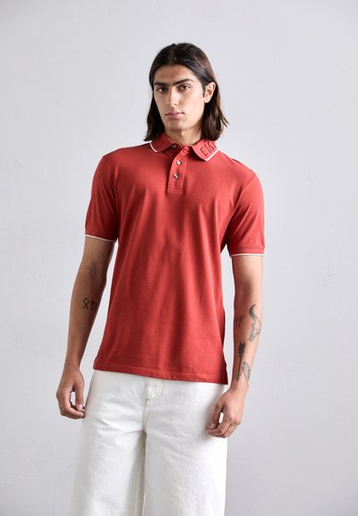 Polo rosso in cotone, con colletto a coste con rifiniture a contrasto, patta con tre bottoni e logo ricamato sul colletto.
