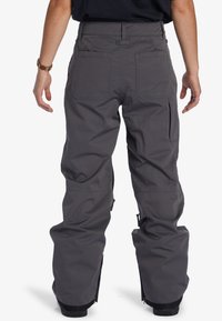 Grå snowboardbyxor med lös passform, flera fickor, dragkedjor vid anklarna och en slät, hållbar tygkvalitet.