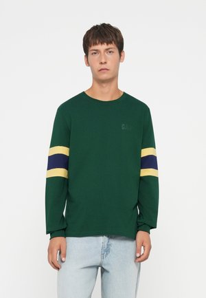 Green long-sleeve t-shirt made of cotton, featuring yellow and blue horizontal stripes on sleeves, with logo printed subtly on chest.