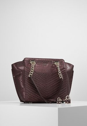 Bordeauxrode tote bag met reliëf logopatron, gouden kettinghengsels en twee kleine hangslotjes aan de voorkant op een wit oppervlak geplaatst.
