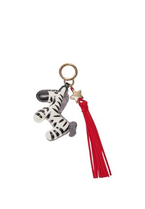 Brelok z figurką zebry w czarno-białe pasy, złotym zawieszką w kształcie gwiazdy oraz długim czerwonym chwostem zwisającym z złotego pierścienia.