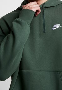 Grön Nike-hoodie med framficka, dragsko i huvan och broderad logotyp i vitt. Mjuk, strukturerad tyg med ribbad mudd.