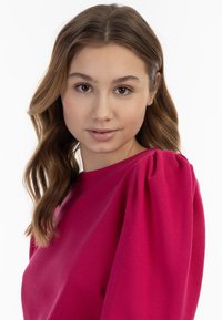 Camisa de manga larga de color rosa intenso con cuello redondo y mangas abullonadas. Textura suave con una tela ligera. Diseño simple, sin patrones ni acentos.