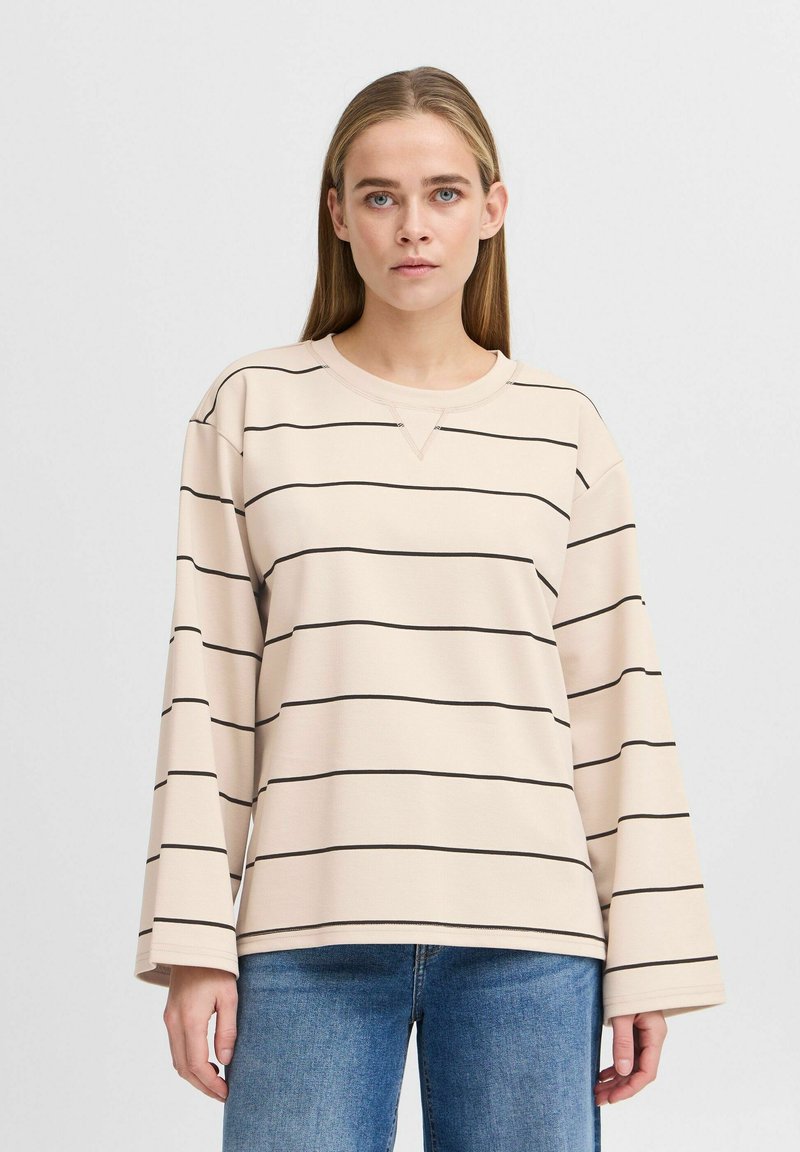 Top beige à manches longues avec des rayures horizontales noires, col rond et coupe décontractée. Le tissu semble doux avec une texture lisse.