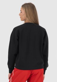Felpa nera con maniche lunghe, scollatura rotonda e polsini a costine, indossata con pantaloni rossi, che mostrano un design semplice e casual.