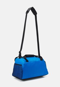 Sac de sport bleu en tissu durable, avec un panneau latéral en mesh, une sangle noire et une poignée supérieure. Forme rectangulaire avec fermeture éclair.