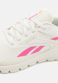 Weiße Reebok-Sneaker mit pinkem Logo, Netz-Obermaterial, weißen Schnürsenkeln und strukturiertem Profil, seitlich betrachtet.