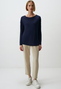 Marineblaues Langarmoberteil mit Rundhalsausschnitt, kombiniert mit beigen, verjüngten Hosen und weißen Sneakers. Glatter Stoff und legere Passform.