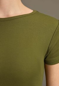Olijfgroene geribbelde t-shirt, korte mouwen, ronde halslijn en een gladde textuur. Bevat subtiele stiksels langs de randen.