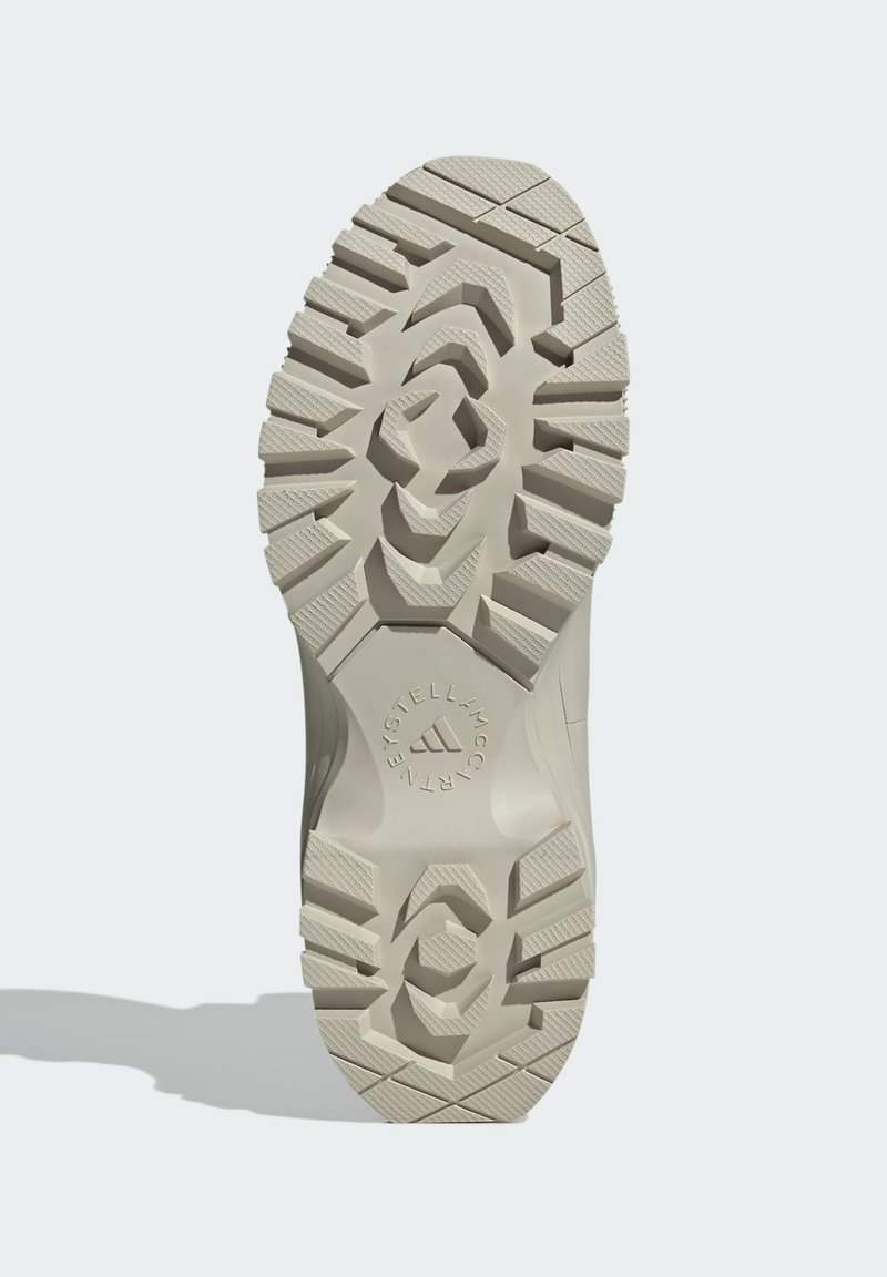 Podeszwa beżowego buta Adidas Stella McCartney z głębokim, wzorzystym bieżnikiem i okrągłym logo na jasnym tle.